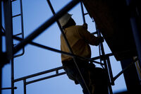 Photo shows a construction worker climbing a scaffold ladder