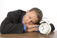 Photo shows a man in a suit sleeping by an alarm clock