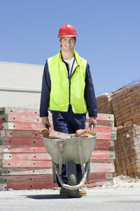 Photo shows a worker moving bricks in a wheelbarrow on a construction site