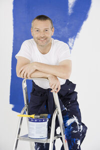 Photo shows a painter standing on a stepladder